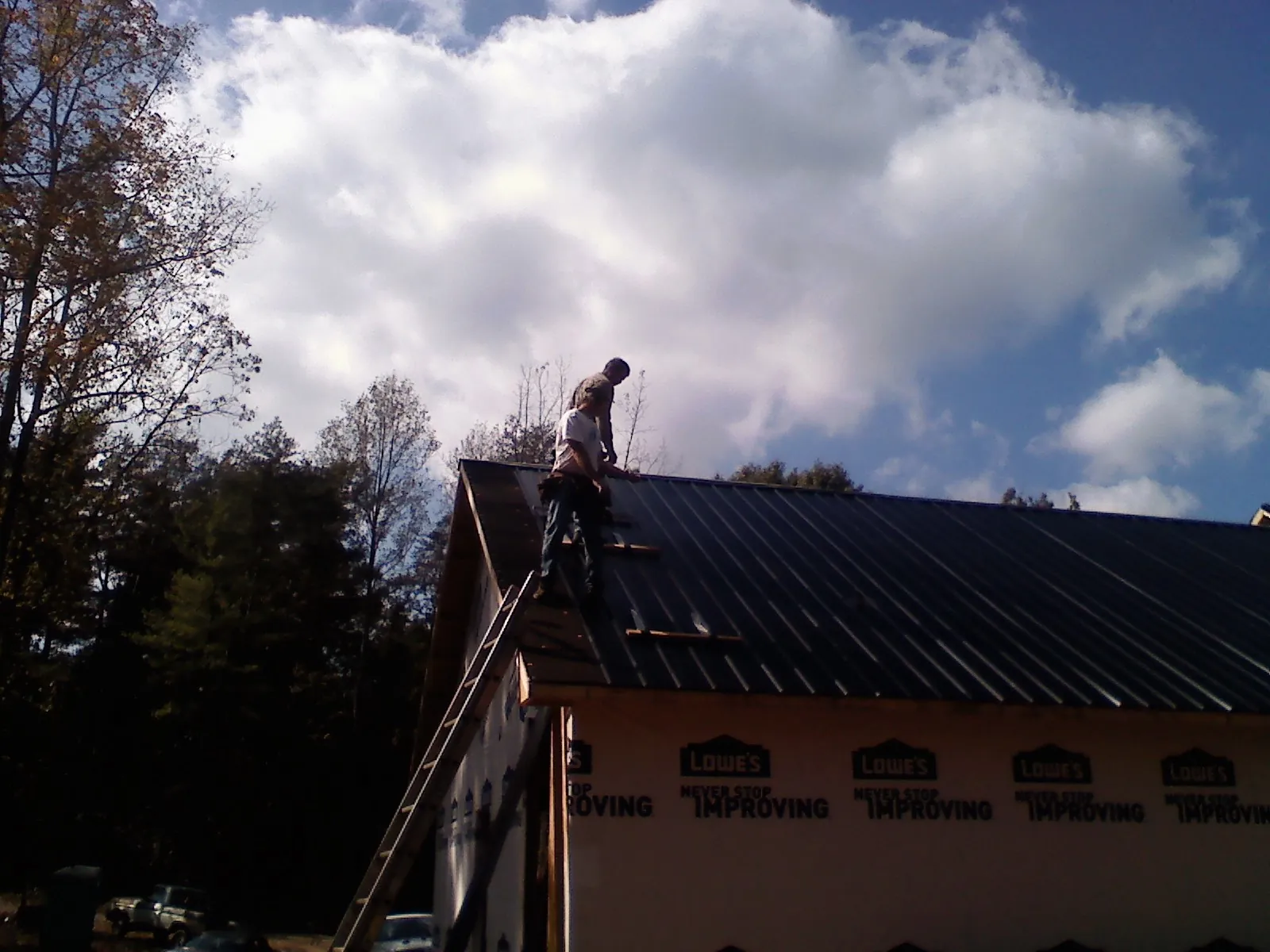 Roofer fastening dark metal panels high against a cloudy sky, from a Roof Inspection job in Swedesboro