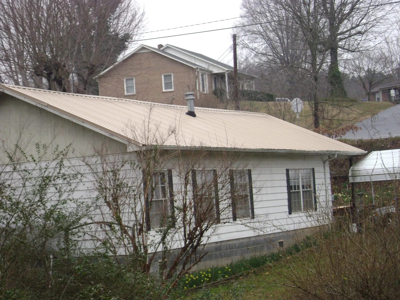 Tan metal roof on a white sided house set into a hillside — Commercial Roofing by Roofing Brothers in Swedesboro